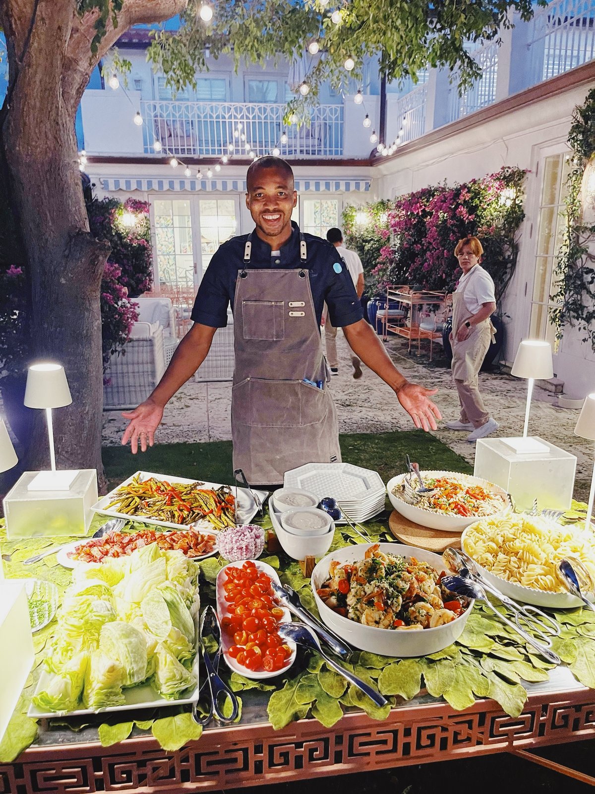 David serving a private event buffet in a flower-lined courtyard